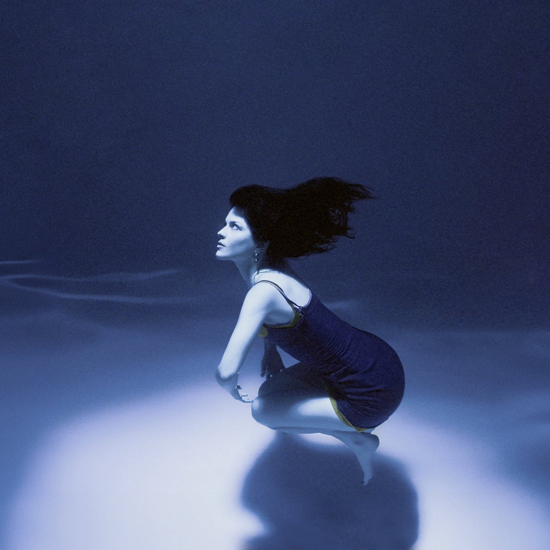 Woman in dress underwater with flowing hair, surrounded by blue light, serene aquatic scene