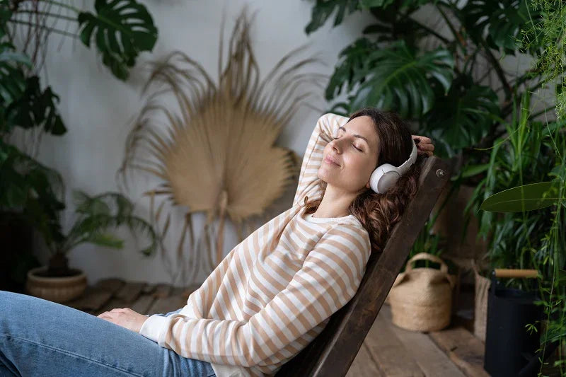 Relaxed young woman wearing headphones, enjoying music in a cozy indoor garden setting