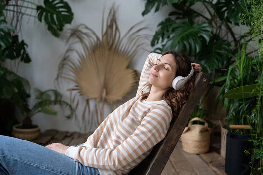 Relaxed young woman wearing headphones, enjoying music in a cozy indoor garden setting