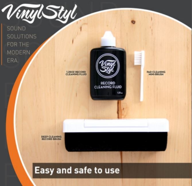 Vinyl record cleaning kit with fluid, mini brush, and record brush on wood background.
