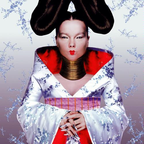 A person wearing a white and red patterned kimono, with elaborate hair and gold neck rings, poses with hands clasped against a light, snowflake-patterned background.