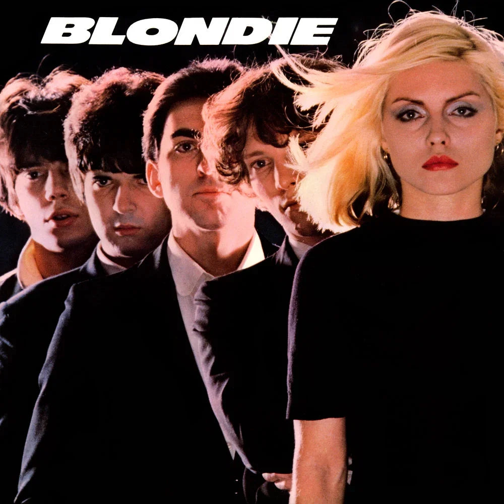Six people stand in a diagonal line against a black background, with a blonde woman in front. "BLONDIE" is written in bold white letters at the top.