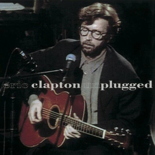 A man with glasses plays an acoustic guitar and sings into a microphone; text over the image reads "eric clapton unplugged.