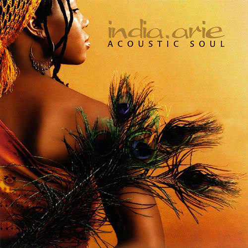 A woman with braided hair and an orange headwrap holds peacock feathers against her bare back; text reads "india.arie ACOUSTIC SOUL" on an orange background.