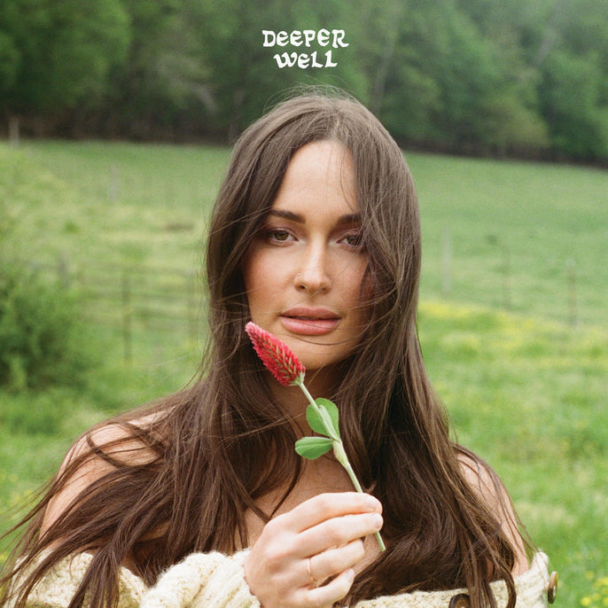 Woman with long brown hair holding a red wildflower in a green field, 'Deeper Well' text above.