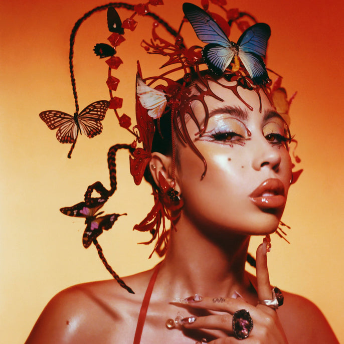 Woman with artistic butterfly headpiece, glossy makeup, and glowing orange background