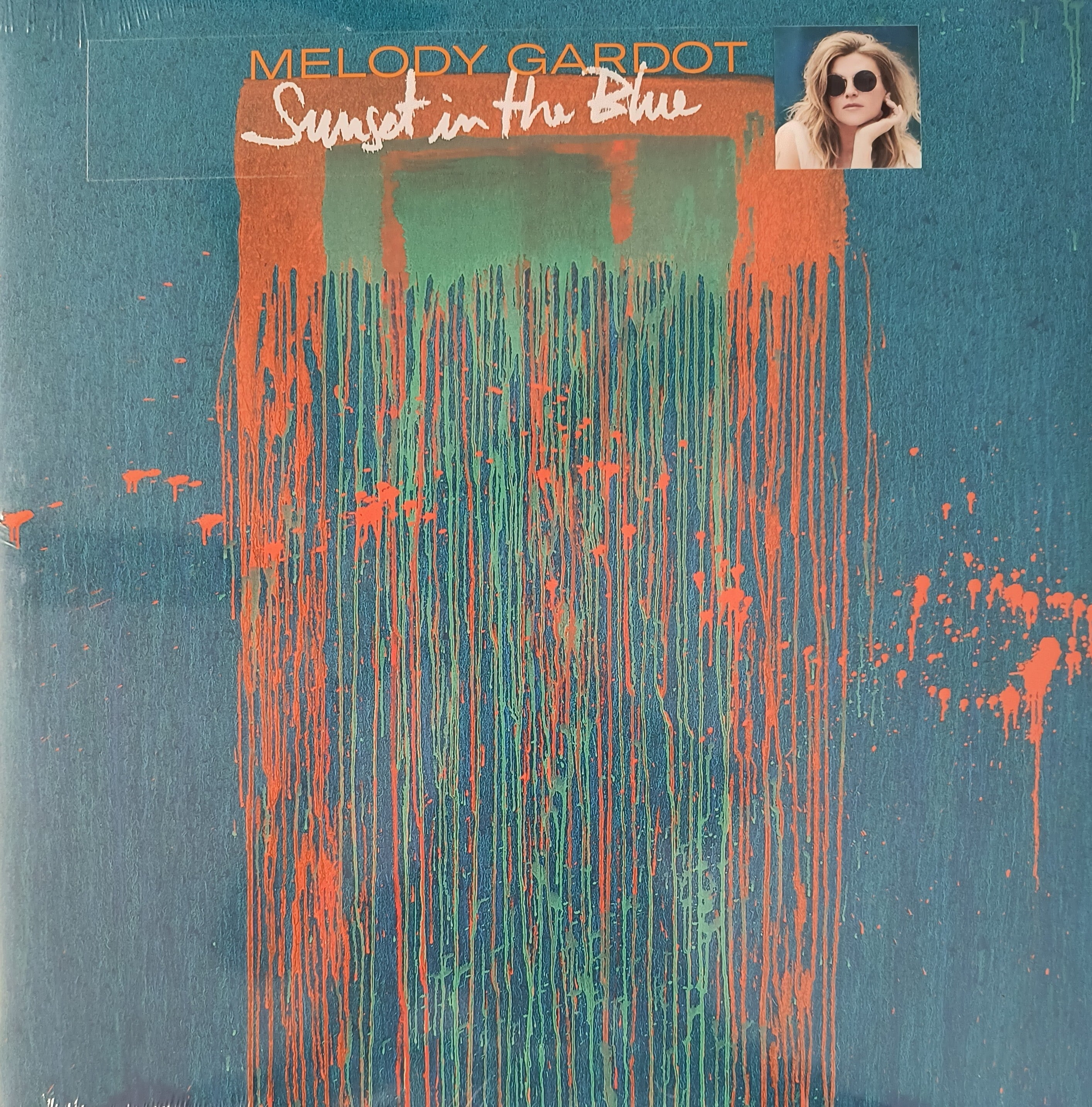 Album cover for "Sunset in the Blue" by Melody Gardot, featuring abstract orange and green paint streaks on a blue background with a small photo of the artist in the top right corner.