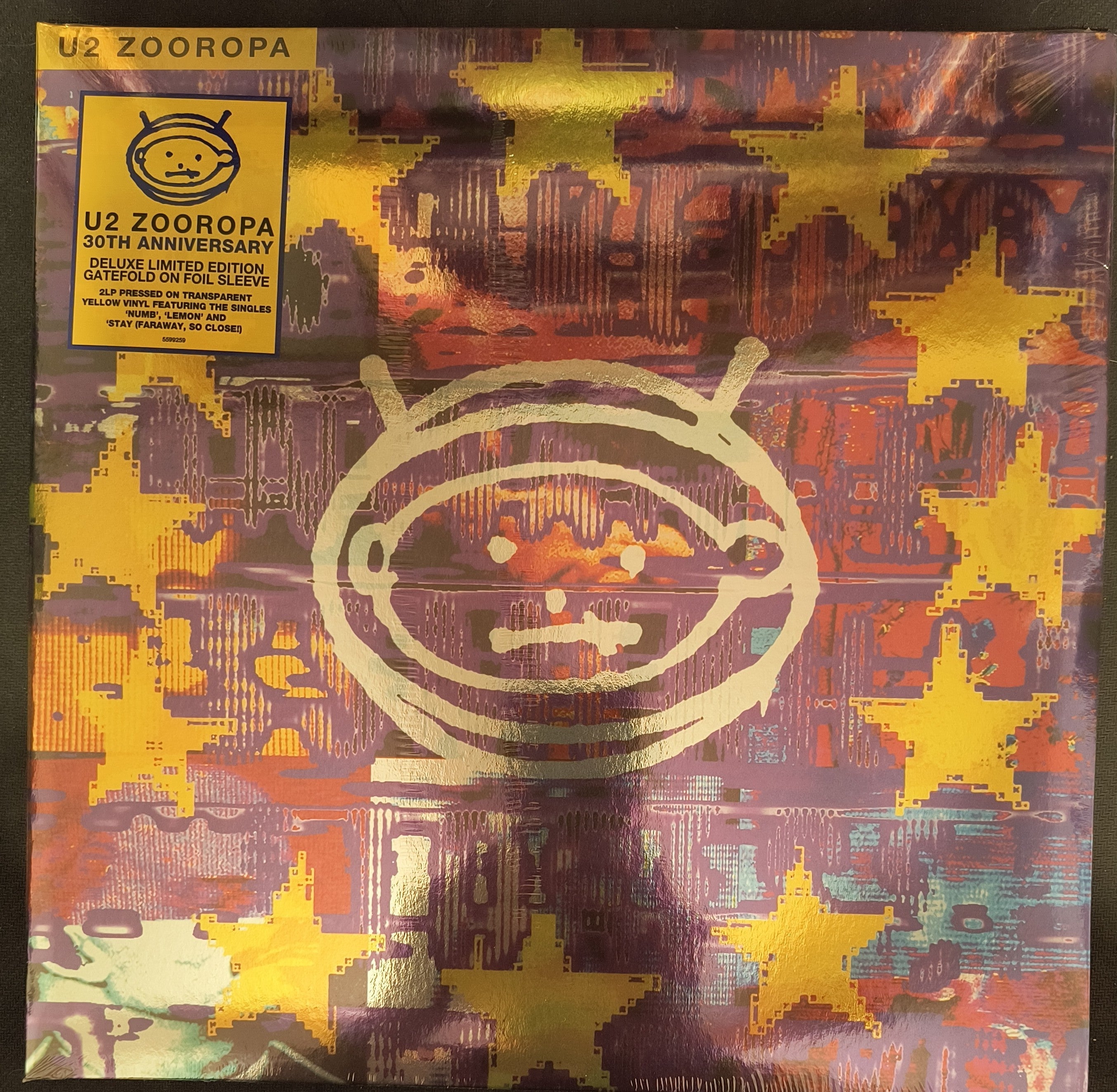 The album cover for U2's "Zooropa" 30th Anniversary edition features a stylized alien face and yellow stars on a colorful, abstract background with a yellow sticker detailing the edition.