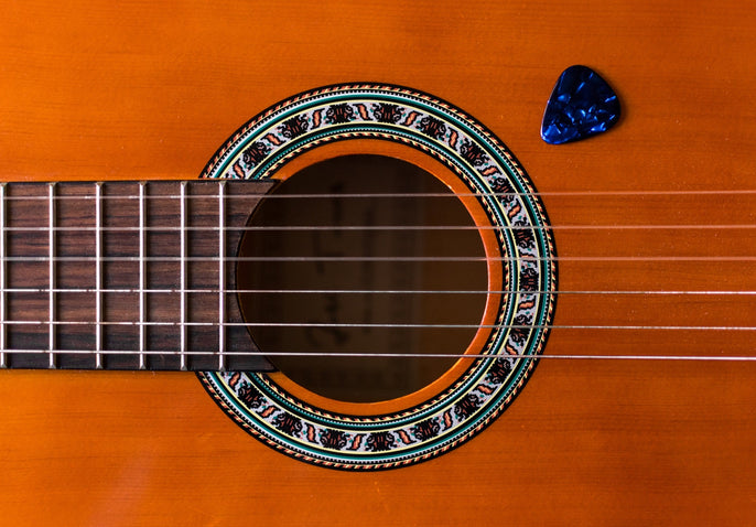 Close-up of classical acoustic guitar strings, wooden body, and blue guitar pick.