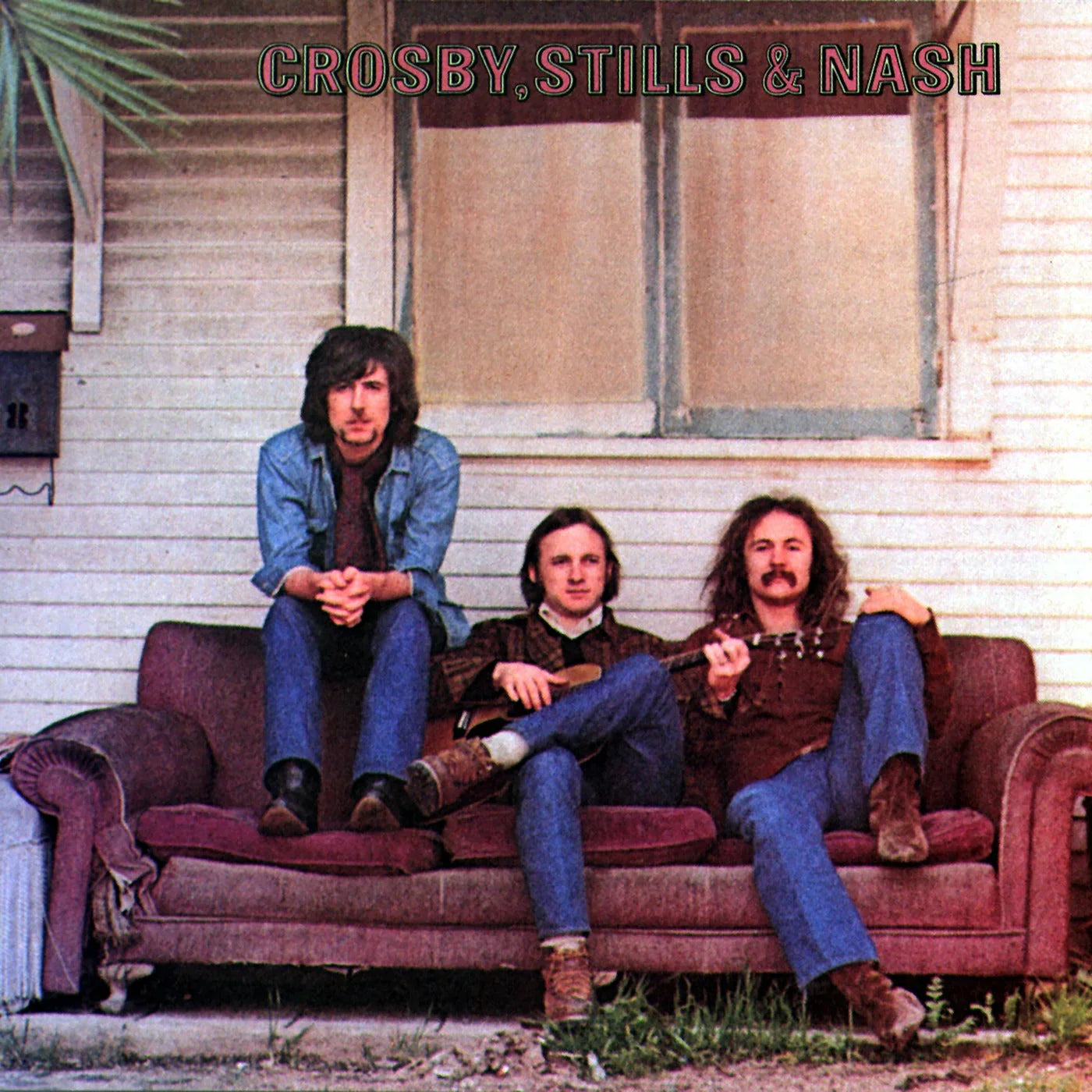 Three men sit on an old couch outside a wooden house under a window; the album title "Crosby, Stills & Nash" is written at the top.