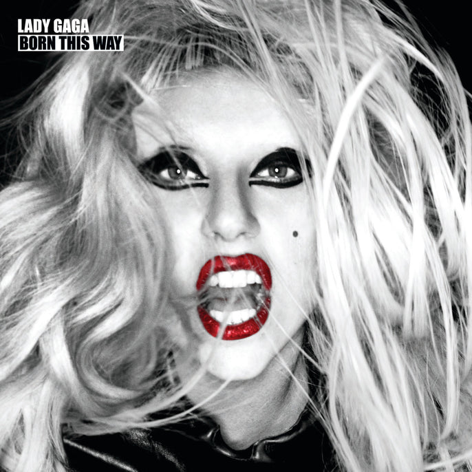 Black and white close-up of a person with wild blond hair, bold eye makeup, bright red lipstick, and an open mouth, with "LADY GAGA BORN THIS WAY" text in the top left corner.