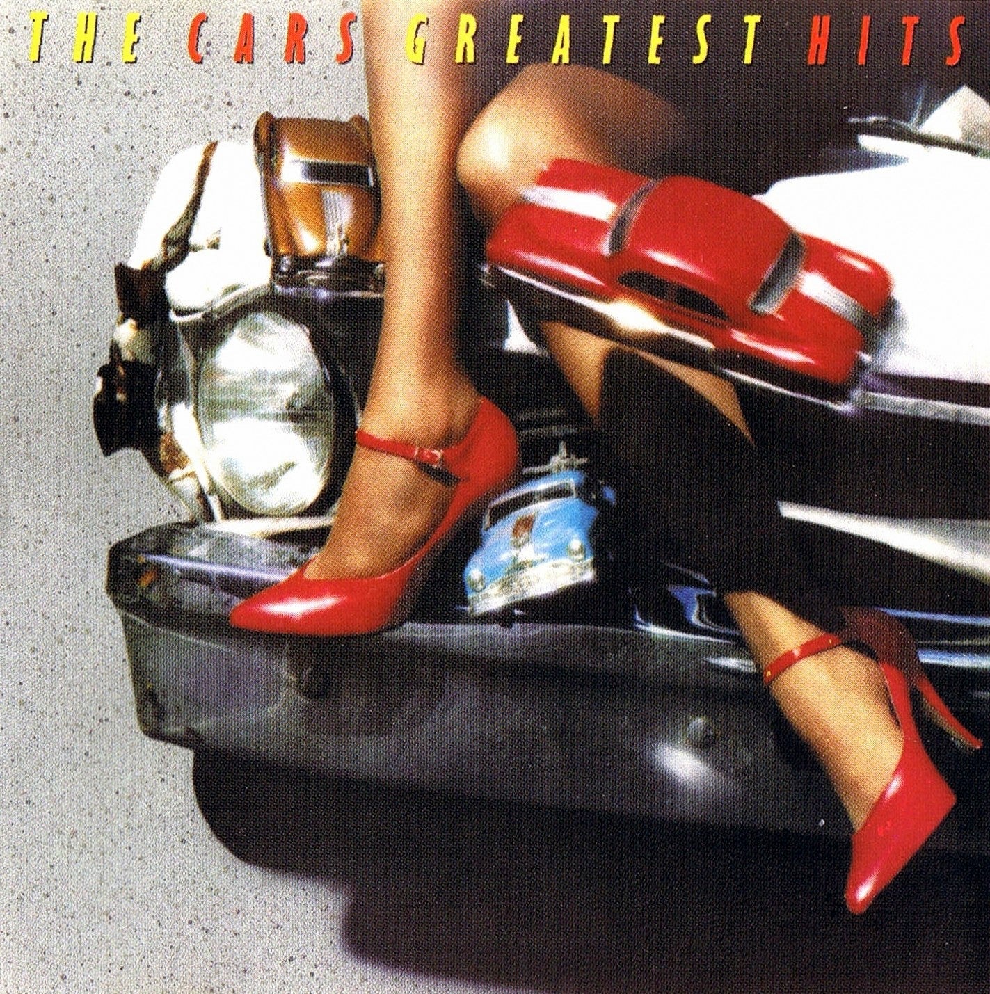 Album cover for "The Cars Greatest Hits" showing a person's legs in red high heels resting on a vintage car’s bumper, with a toy car nearby.