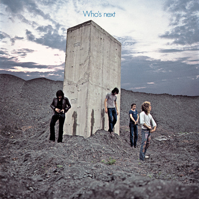 Four men stand around a large concrete slab in a barren landscape under a cloudy sky with the words "Who's next" at the top.