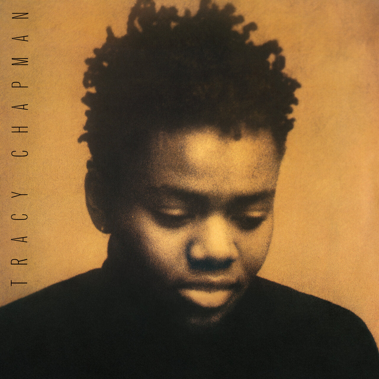 A sepia-toned portrait of a person with short, textured hair looking downward, set against a plain background. The text "Tracy Chapman" is written vertically along the left side.