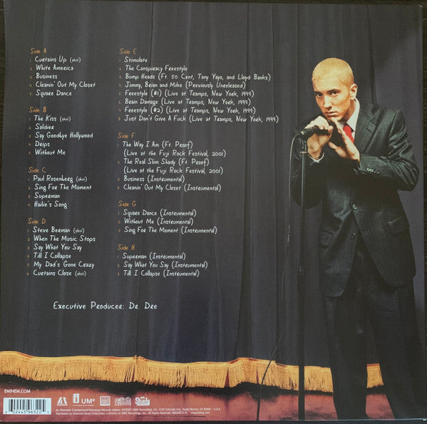 Blonde man in black suit holding microphone on stage next to vinyl record tracklist and credits.