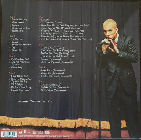 Blonde man in black suit holding microphone on stage next to vinyl record tracklist and credits.
