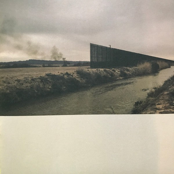 Vinyl record cover with a rural landscape, canal, and tall fence under cloudy sky