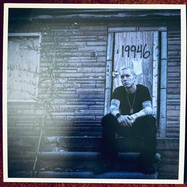 Tattooed man sitting on porch steps in front of a boarded house with street number 19946