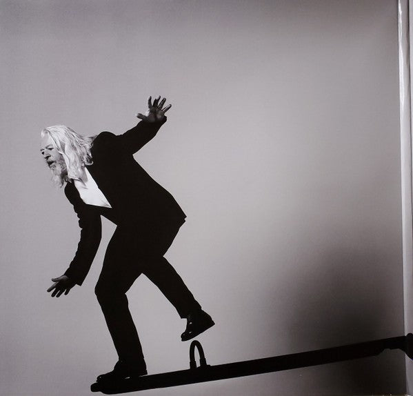 Man with long white hair in black suit balancing on a seesaw, grayscale artistic photo
