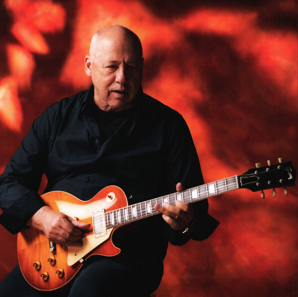 Bald man in black shirt playing electric guitar with orange sunburst finish, red abstract background