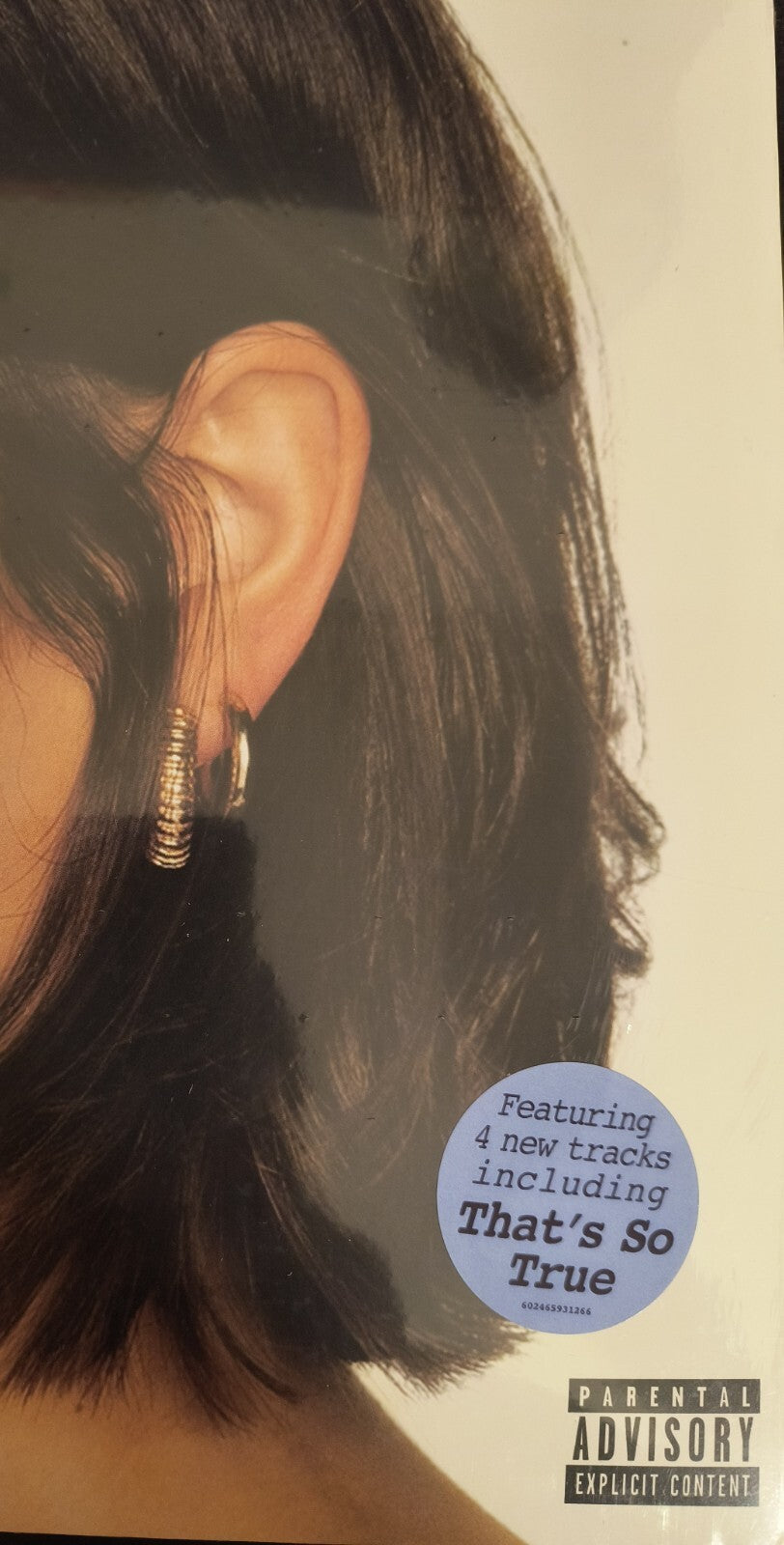 Close-up of a woman's ear with gold hoop earrings, vinyl record cover sticker with track info, parental advisory label