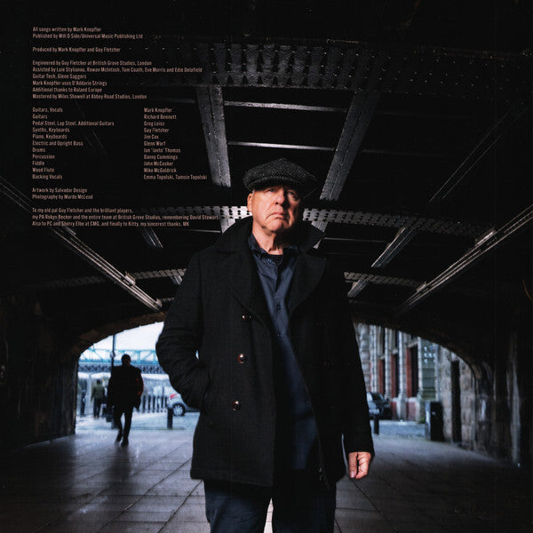 Man in dark coat and flat cap standing under city bridge, urban vinyl record cover style