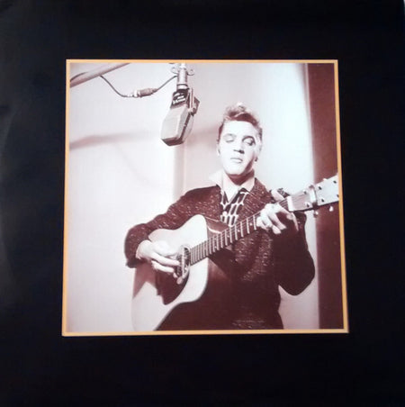 Vintage black and white photo of a musician playing acoustic guitar and singing into a studio microphone.