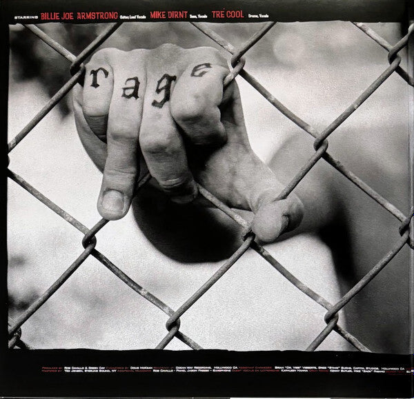 Black and white photo of hand gripping chain link fence with 'rage' tattooed on fingers.