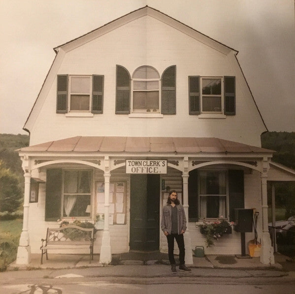 Man standing in front of a vintage town clerk's office with white siding and green shutters