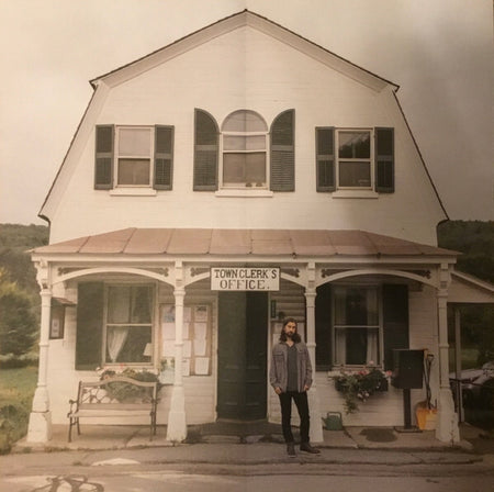 Man standing in front of a vintage town clerk's office with white siding and green shutters