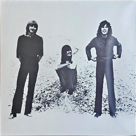 Black and white photo of three men, two standing and one sitting on gravel, classic rock vinyl cover