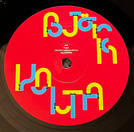 Close-up of Björk vinyl record with bold red label and colorful geometric text design.