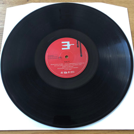 Black vinyl record with red center label on white sleeve, wooden surface background