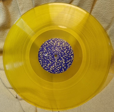 Yellow translucent vinyl record with blue and yellow speckled center label on fabric