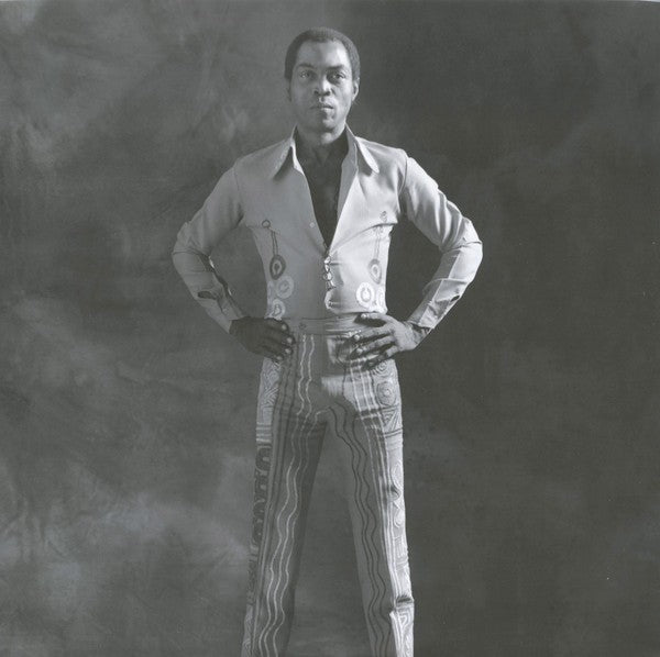 Black and white photo of a man in patterned pants and vintage shirt, standing confidently.