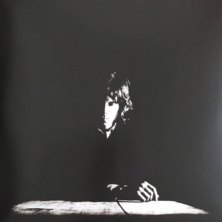 Black and white album cover with solitary figure in dramatic lighting at a table